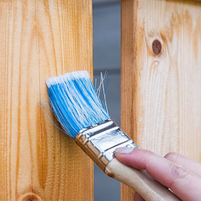 a person's hand painting a wooden fence with a blue brush